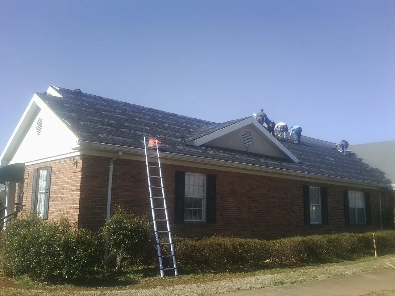 Crew tearing shingles off a brick ranch roof with a ladder set — Emergency Roof Repair work by our crew in Artemas