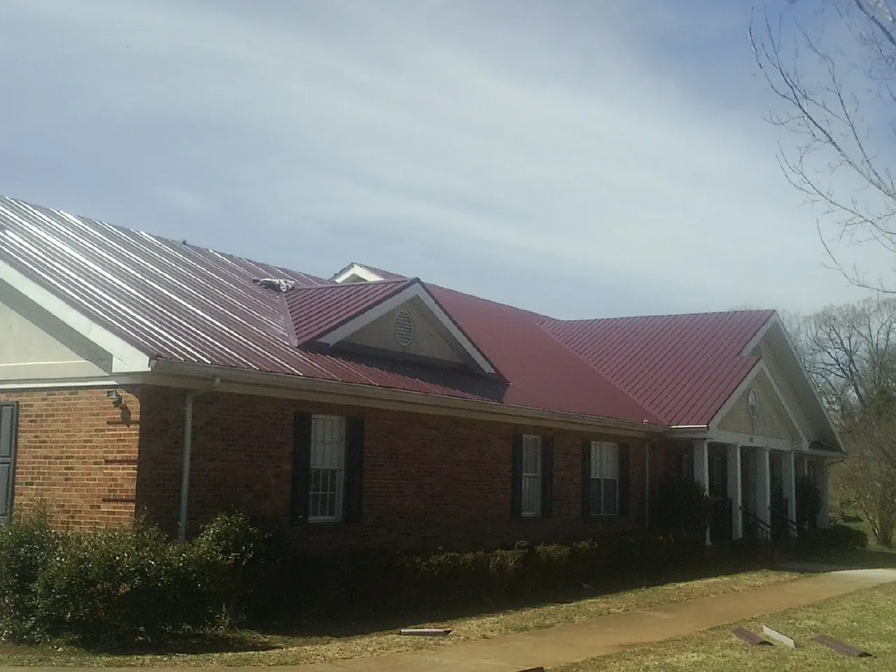 Red metal roof with gabled entries on a long brick building, from a Hail Damage Roof Repair job in Artemas