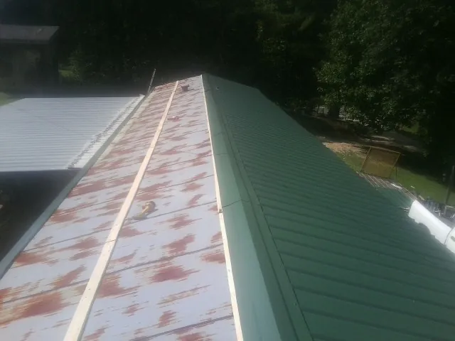 Old rusted panels beside newly installed green metal roofing — Wind Damage Roof Repair by Roofing Brothers in Artemas