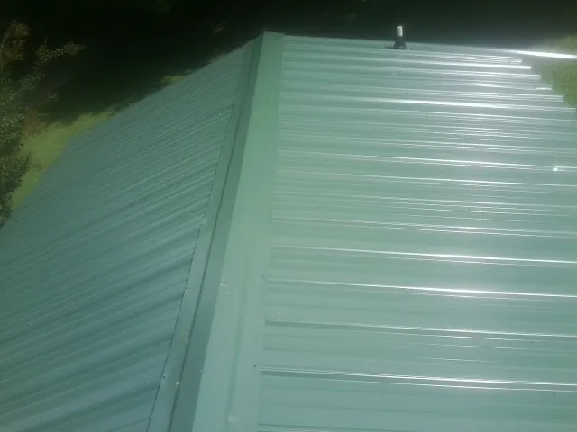 New green metal panels meeting at the ridge of a roof — Flat Roof Repair work by our crew in Artemas