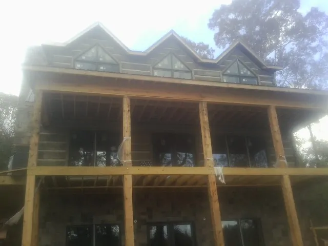 Dormers and porch framing on a large log home under construction — Roof Coating work by our crew in Artemas