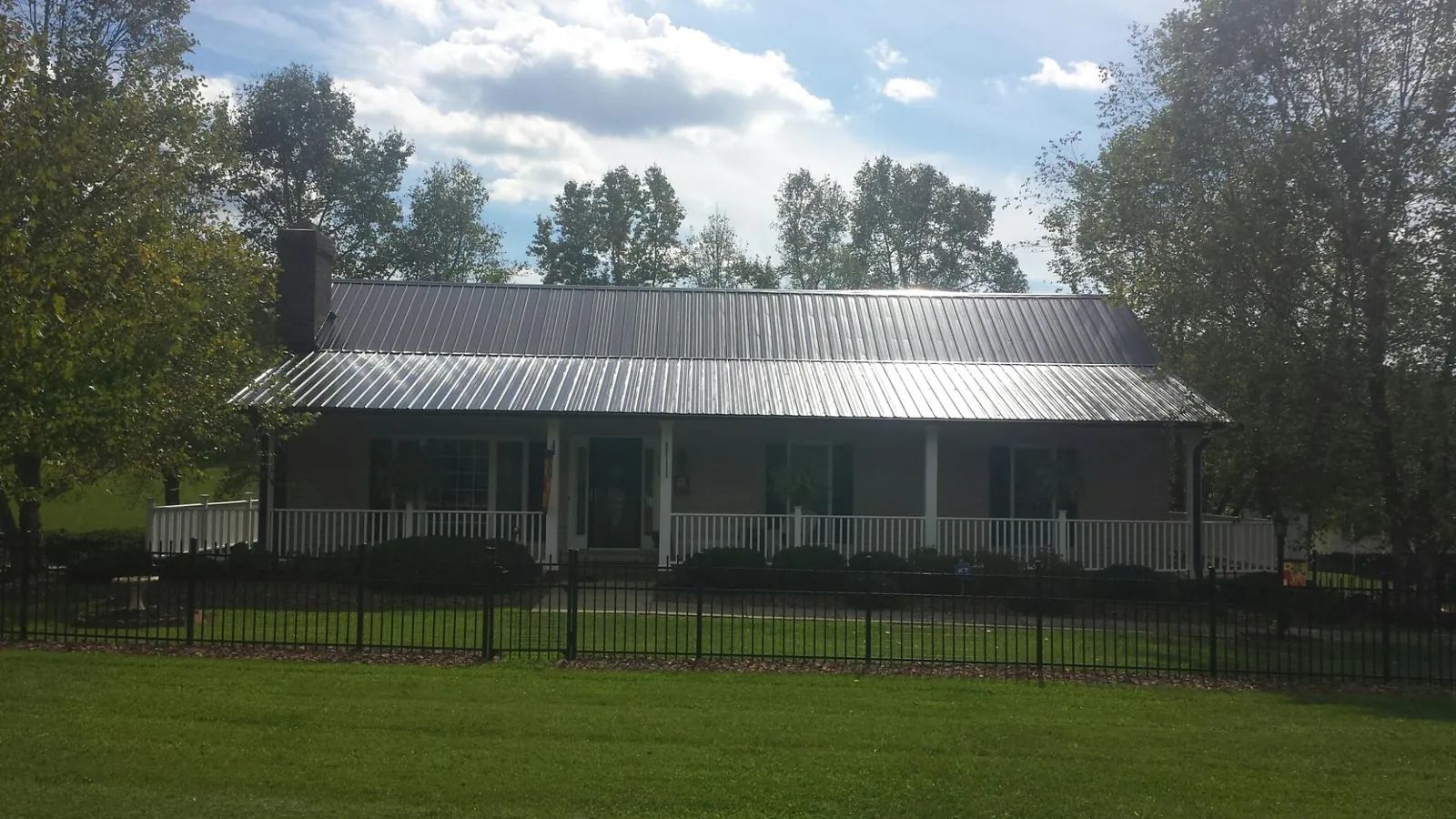 Gray metal roof on a brick ranch with a full width front porch — Gutter Guard Installation work by our crew in Artemas