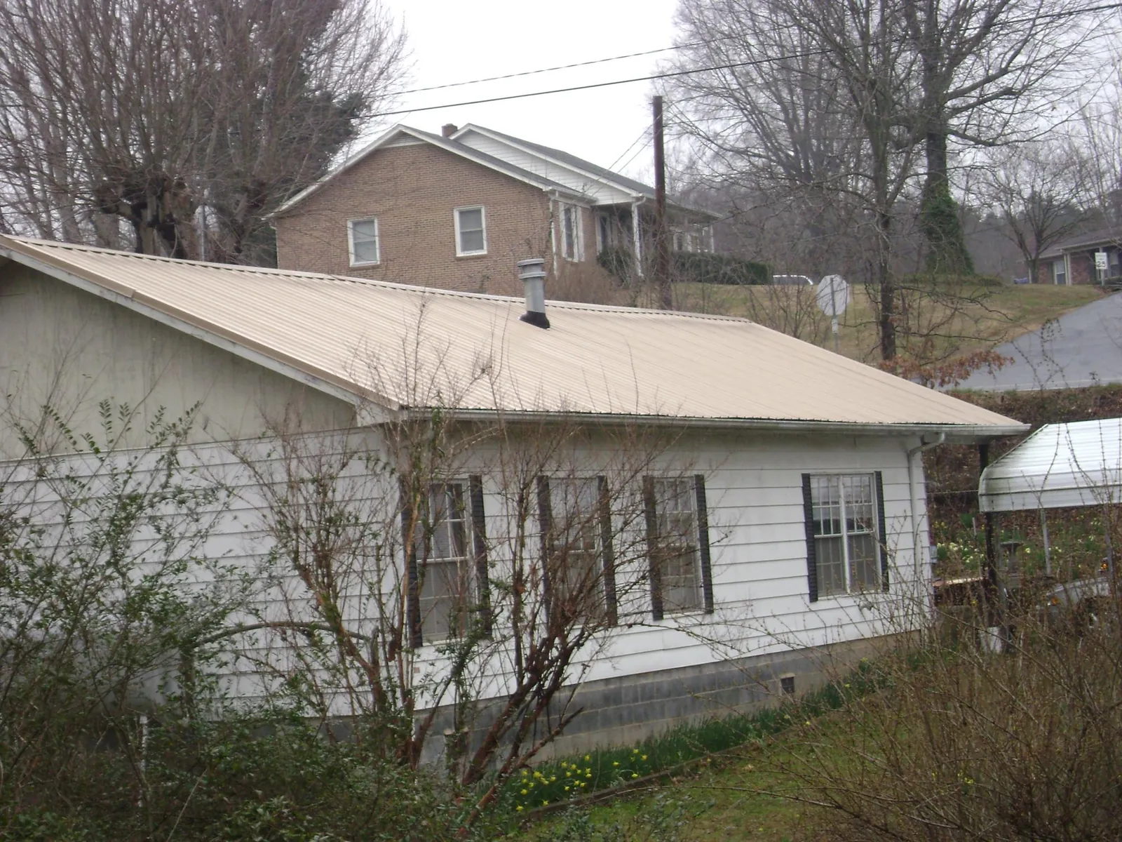 Tan metal roof on a white sided house set into a hillside — Commercial Roofing by Roofing Brothers in Artemas