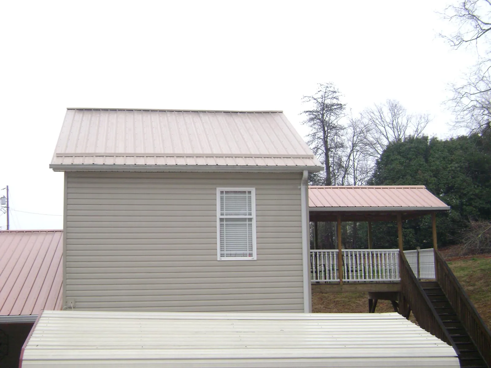 Tan metal roofs on a two story addition and attached porch, from a Roof Replacement job in Artemas
